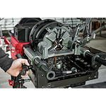 Person operating MX FUEL Pipe Threading Machine with metal pipes and oil shavings visible, showcasing threading process.