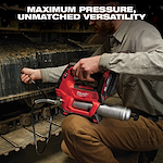 A person using a red Milwaukee cordless grease gun on heavy machinery tracks. The text above reads, "MAXIMUM PRESSURE, UNMATCHED VERSATILITY." The grease gun has a flexible hose and metal barrel, conveying its robust performance.
