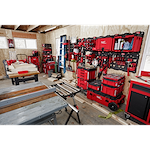 A workshop with tools and equipment organized on red PACKOUT Large Wall Plates, including stacked toolboxes, saws, and hand tools.