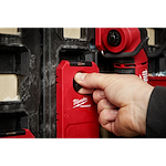 A hand is adjusting the twist dial on the PACKOUT™ Shop Storage Twist Dial Close Up. The red product is mounted on a black wall panel system, featuring prominently a twist-lock mechanism for secure storage.