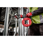 Worker using 1/8" 50' steel fish tape in a construction setting, wearing gloves and a safety vest, guiding tape through conduit.