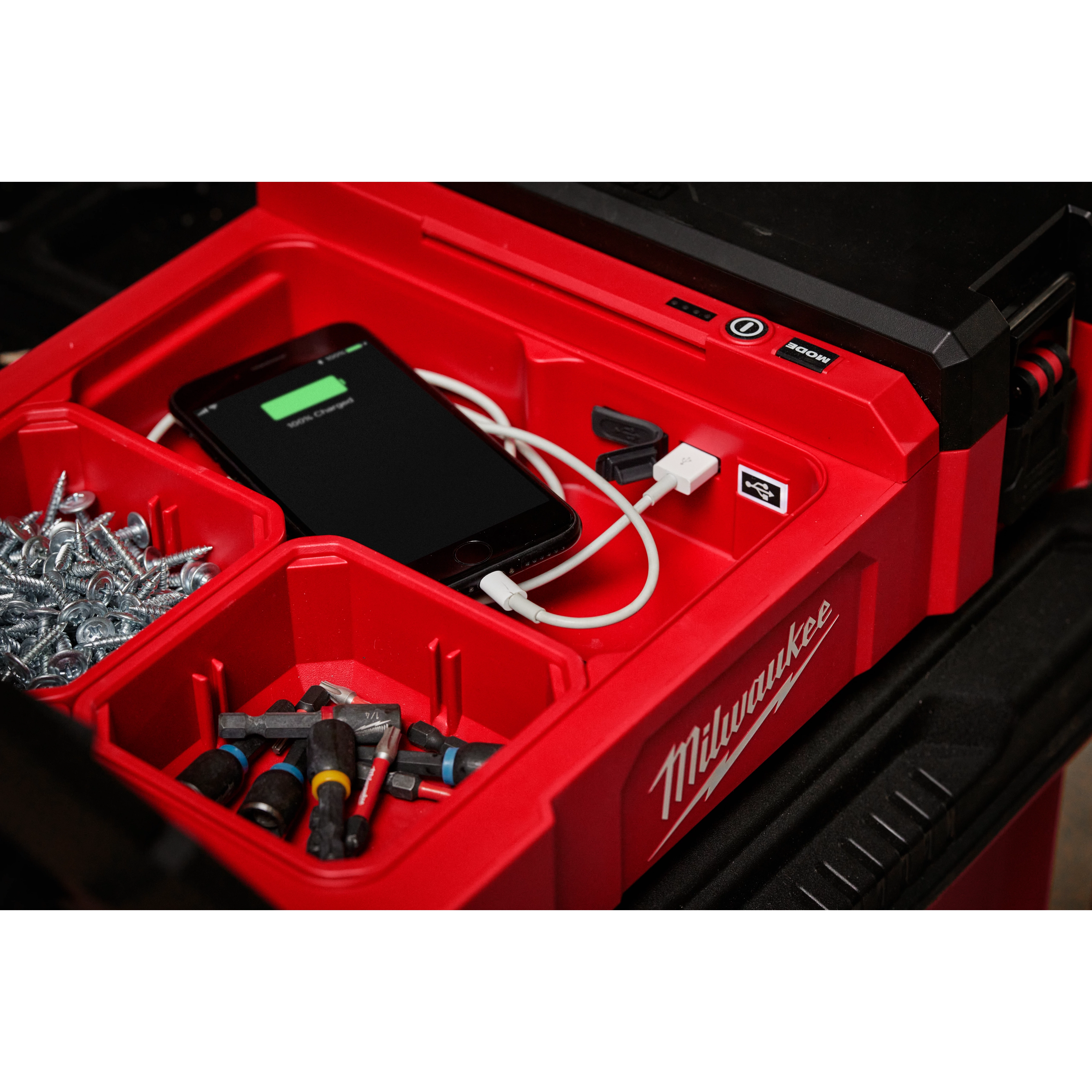 M12 PACKOUT Flood Light with USB Charging shown with various tools, screws, and a phone being charged inside a red tool organizer.