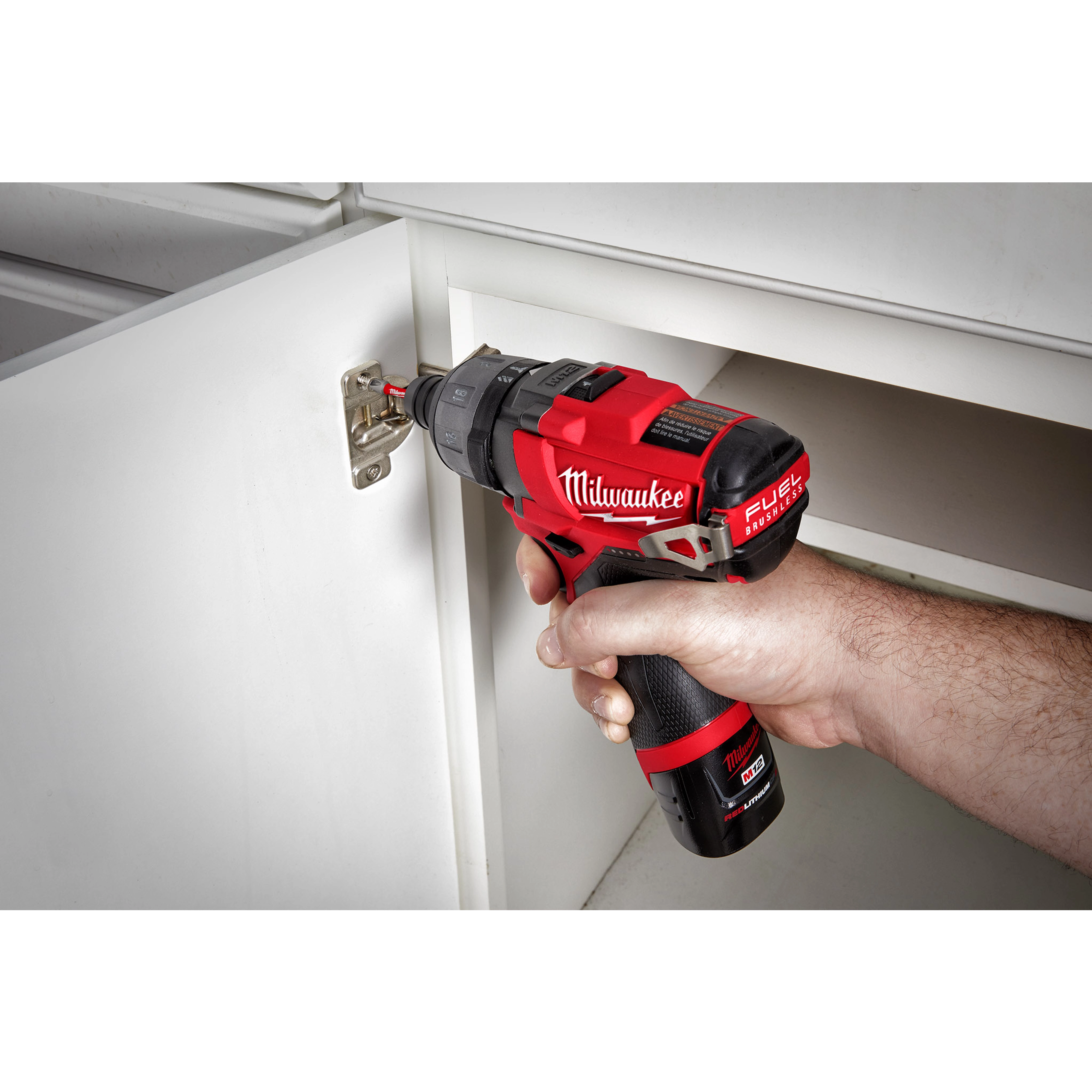 A person uses the M12 Fuel 1/4" Hex 2 Speed Screw Driver, 2402 to tighten a screw on a hinge on a white cabinet door.