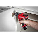 A person uses the M12 Fuel 1/4" Hex 2 Speed Screw Driver, 2402 to tighten a screw on a hinge on a white cabinet door.
