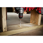 Handheld drill with 1/4" x 4" x 6" SHOCKWAVE Impact Duty Carbide Multi-Material Drill Bit drilling through a wooden plank.