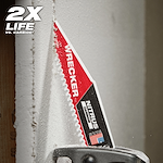 The Milwaukee Wrecker Nitrus Carbide Saw Blade is cutting through dense material. The blade is close to a wooden beam, producing fine dust particles. The text "2X LIFE" is prominently displayed in the top left corner.