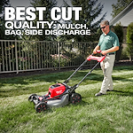A person operates an M18 FUEL™ 21" Self-Propelled Dual Battery Mower on a lawn. The mower is red and black with a silver base. Text reads "BEST CUT QUALITY: MULCH, BAG, SIDE DISCHARGE." Trees and a fence are in the background.