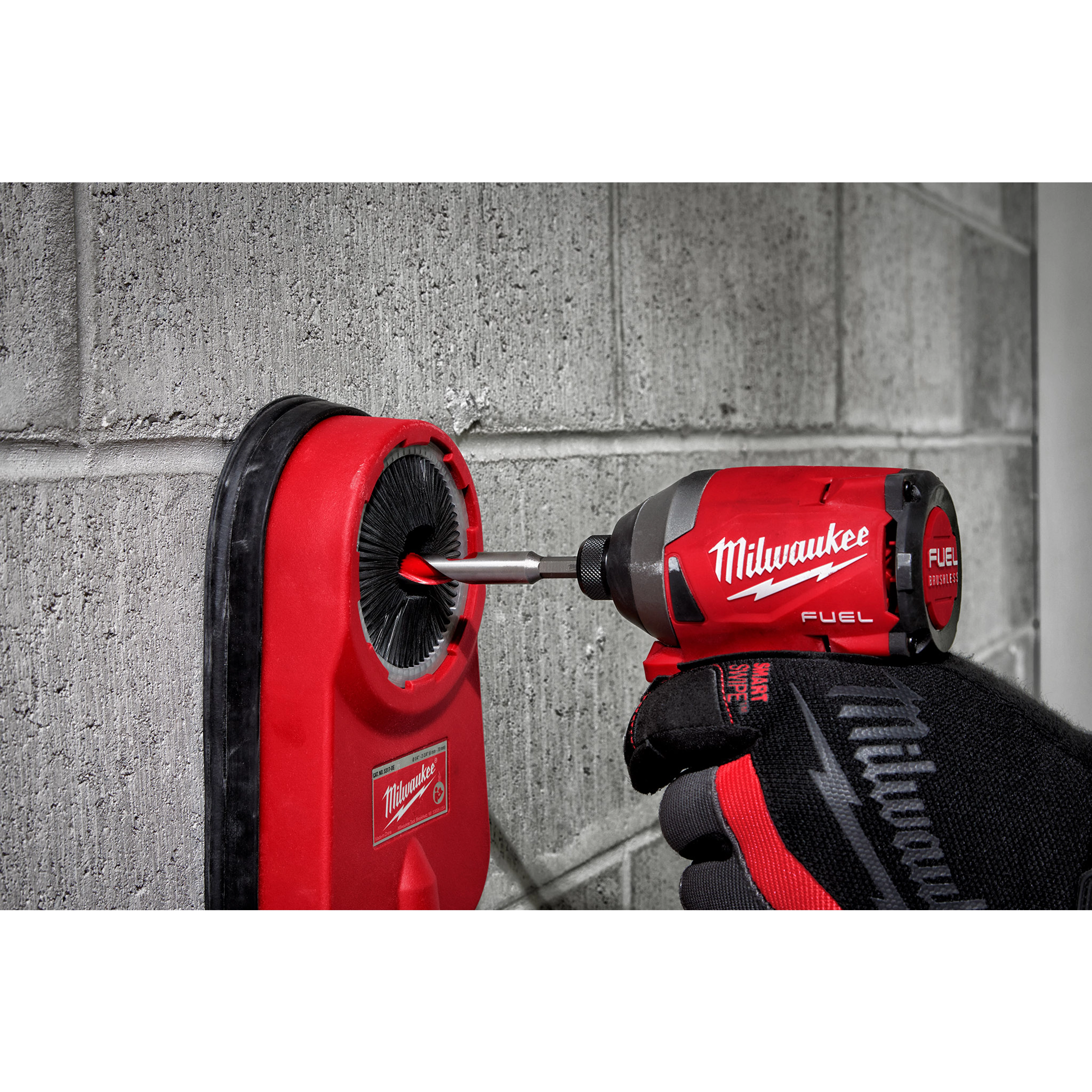 Gloved hand using Milwaukee fuel drill with 1/2" X 4" X 6" Hammer Drill Bit on a concrete wall with red dust collector attached.