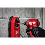 Gloved hand using Milwaukee fuel drill with 1/2" X 4" X 6" Hammer Drill Bit on a concrete wall with red dust collector attached.