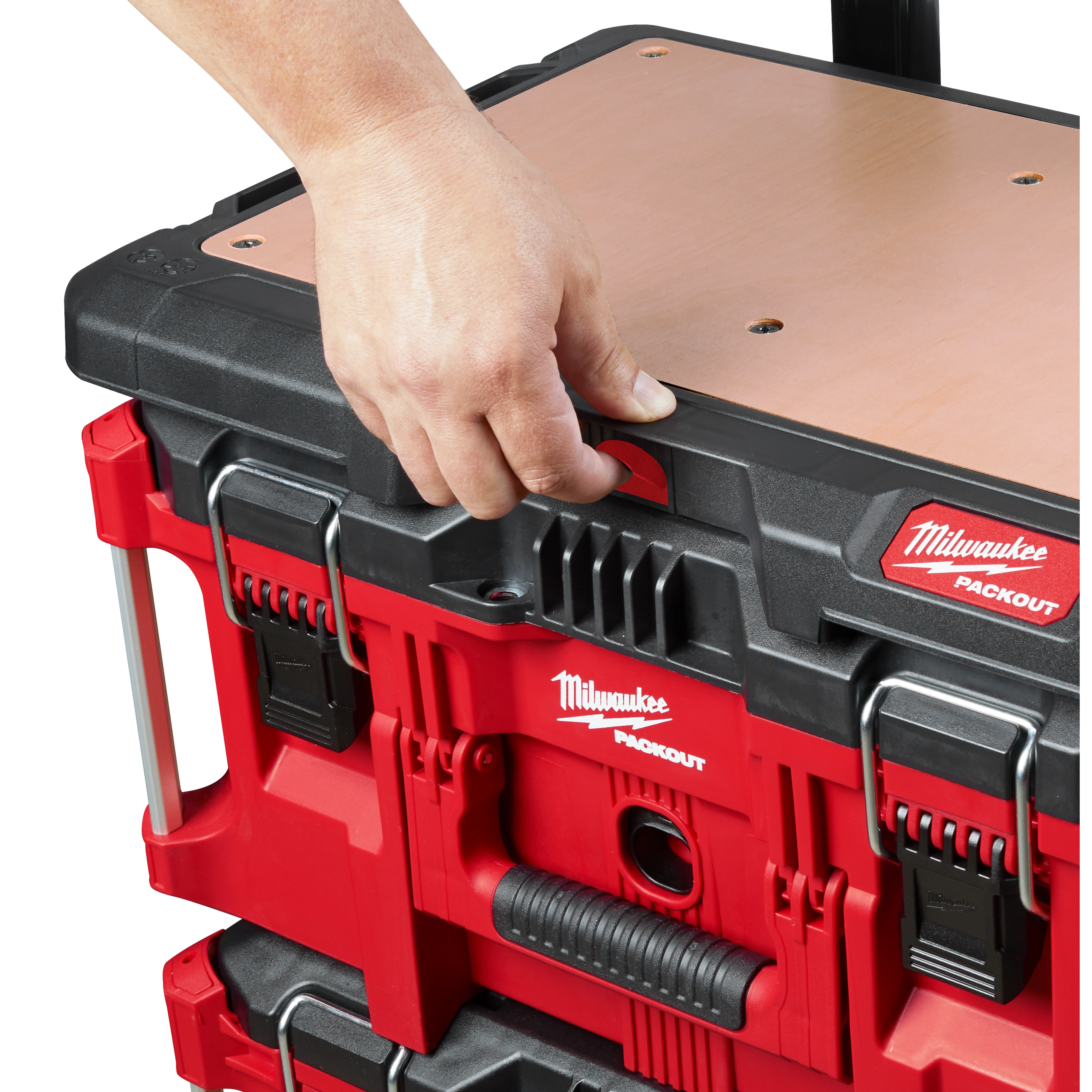 A hand grips the handle of a stacked red and black PACKOUT Customizable Work Top with a wooden surface and metal latches.