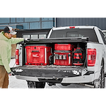A person is loading a PACKOUT™ Rolling Drawer Tool Box and other PACKOUT™ storage boxes into the bed of a white truck on a snowy day.