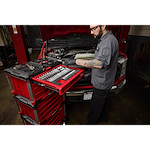 A mechanic works on a car engine using a 366pc. Master Mechanics Hand Tool Set with PACKOUT™ Drawers and Dolly. The tool set is organized in red drawers, with various tools visible on the workbench.