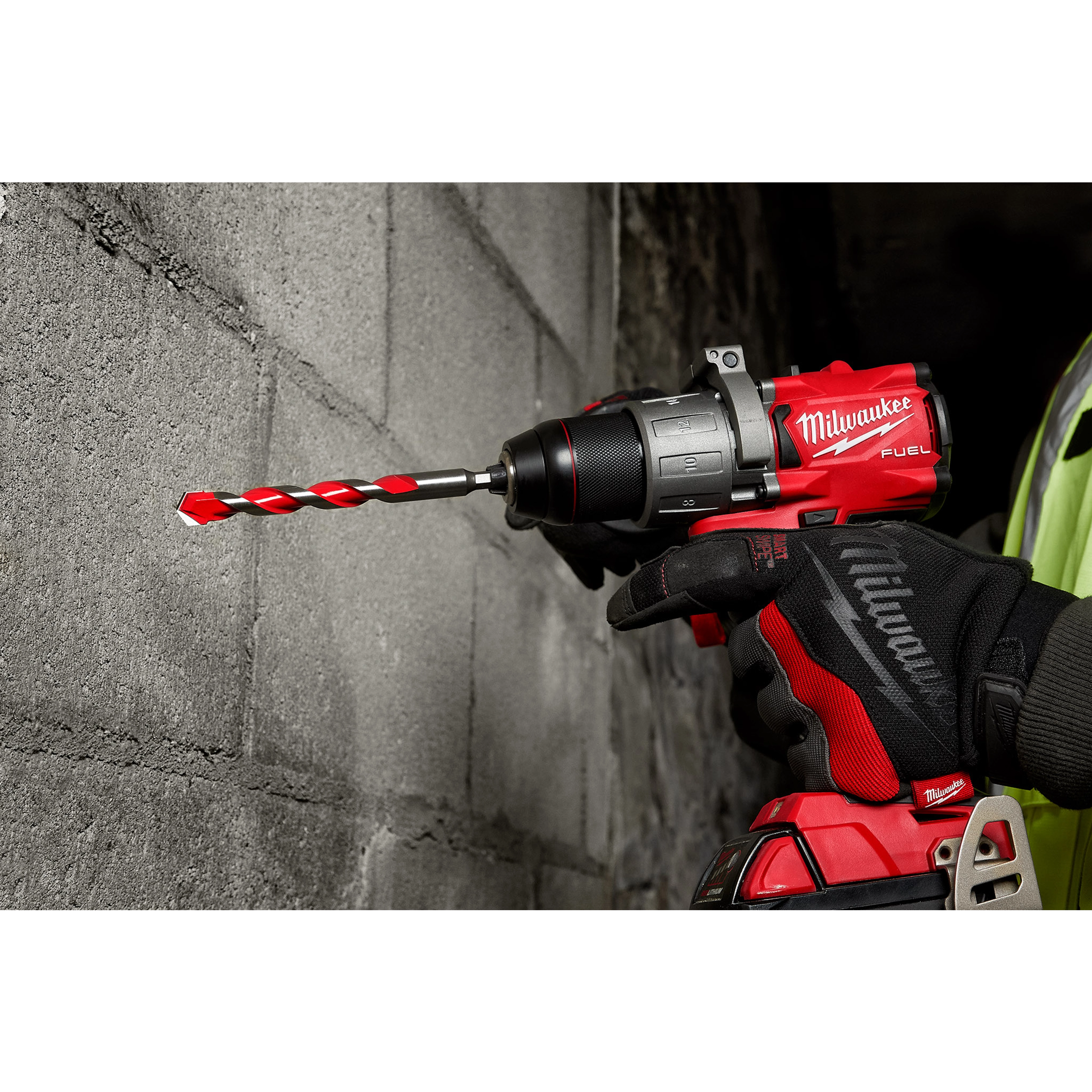 Close-up of a person using a red and black drill with a Shockwave Carbide Hammer Drill Bit, 1/2", drilling into a concrete wall.