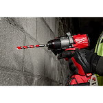 Close-up of a person using a red and black drill with a Shockwave Carbide Hammer Drill Bit, 1/2", drilling into a concrete wall.