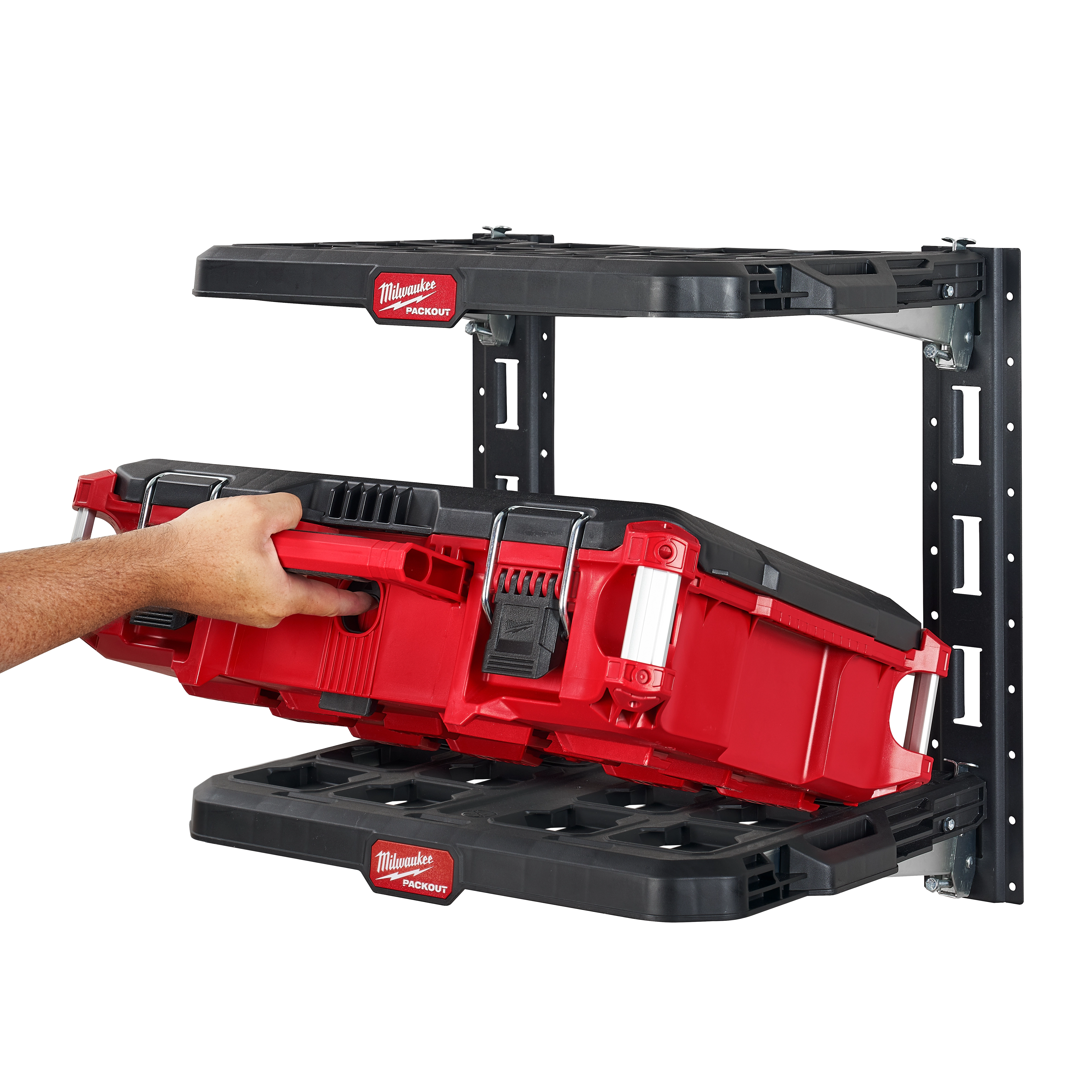 Hand placing a red tool storage box onto the PACKOUT Racking Kit's black shelving, which is mounted on a wall.