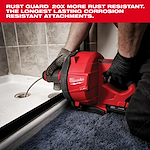 A Milwaukee Fuel drain cleaning tool is being used to unclog a bathroom drain. The red machine is shown in close-up with a worker's gloved hands operating it. Text at the top highlights the Rust Guard feature, stating it is 20 times more rust-resistant.