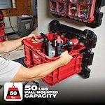 Person mounting a red PACKOUT Mounting Plate holding tools, rated for a 50 lbs wall-mounted capacity, onto a wall.