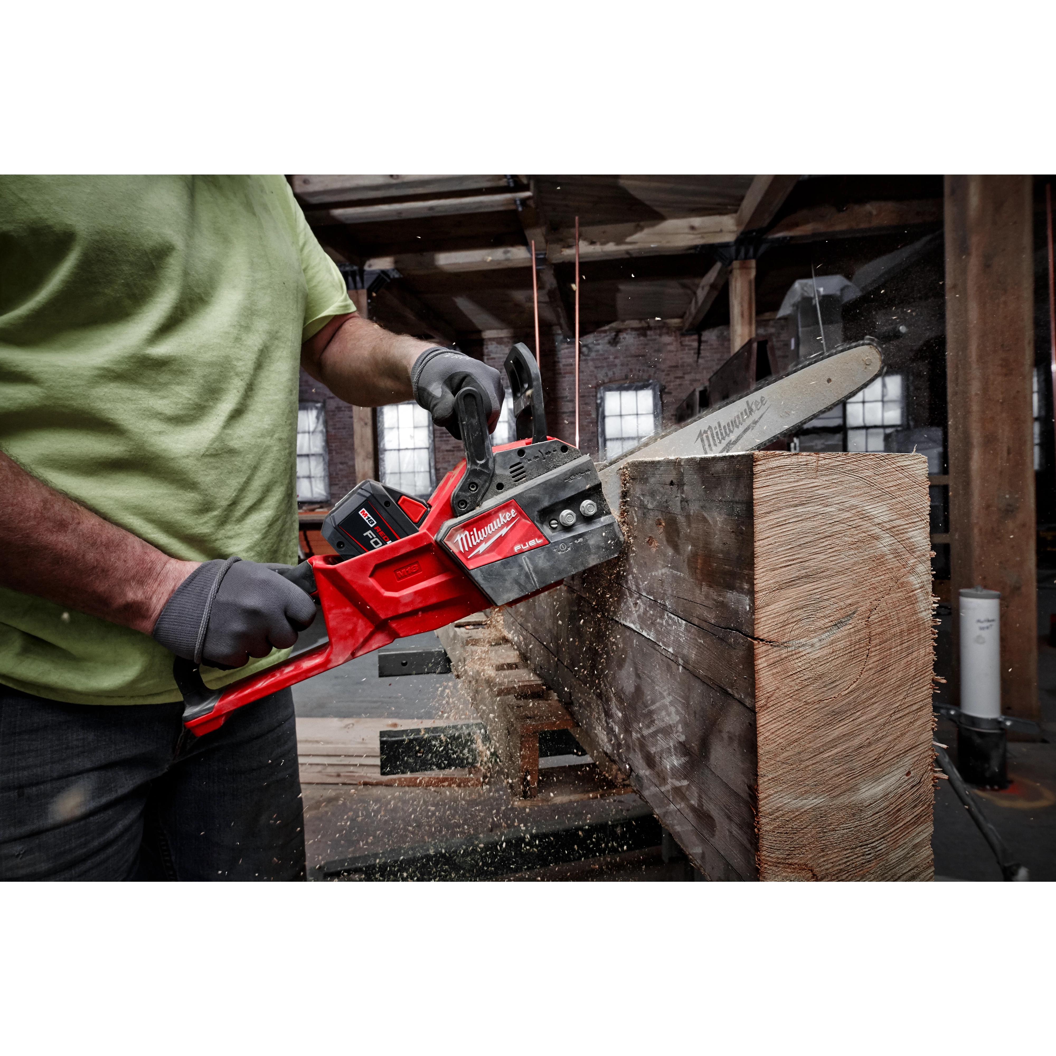 Person in a workshop using a Milwaukee chainsaw to cut a large wooden beam, with sawdust flying.