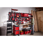 Man organizing tools on a wall-mounted March 2023 Packout Shop Storage system in a well-equipped garage workspace.