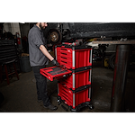 A mechanic is using a 366pc. Master Mechanics Hand Tool Set with PACKOUT™ Drawers and Dolly in a garage. The red tool chest is on wheels and has multiple drawers filled with tools.